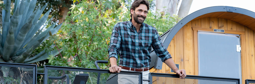 Male model wearing a blue checked button down shirt standing on a railing