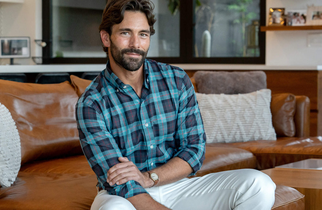 Male model sitting on a leather sofa wearing a button down blue checked shirt