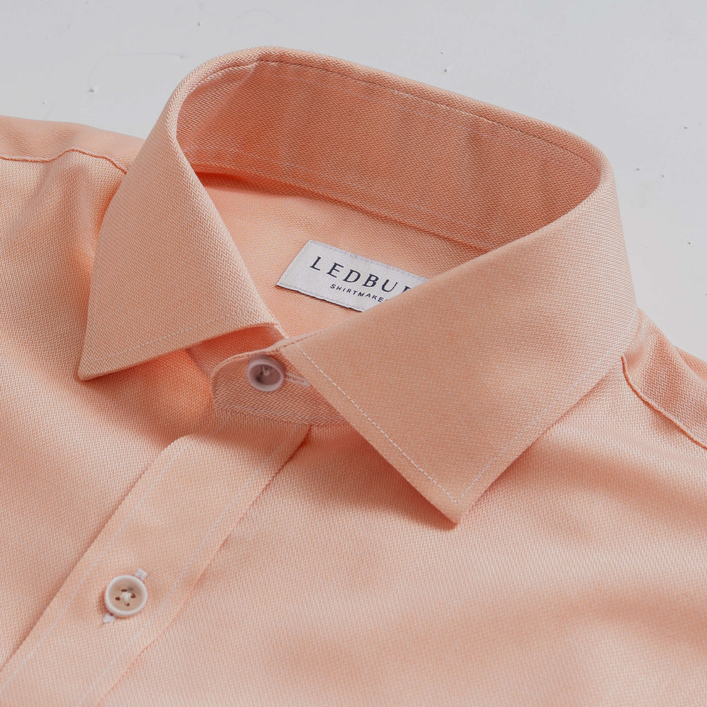 Closeup of the collar of a men's light orange herringbone dress shirt